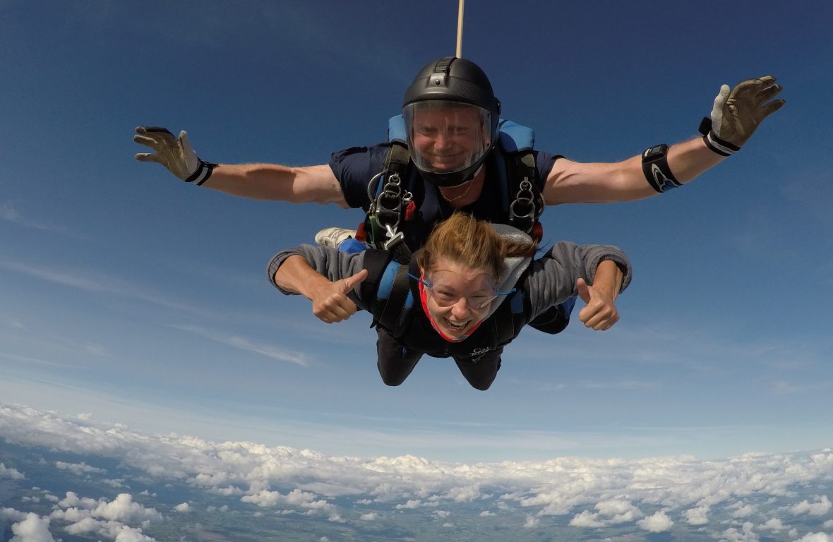 A tandem skydive duo smile as they fall through the sky