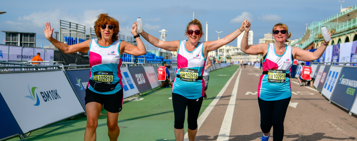 Three female runners hold hands and celebrate running the Brighton marathon together