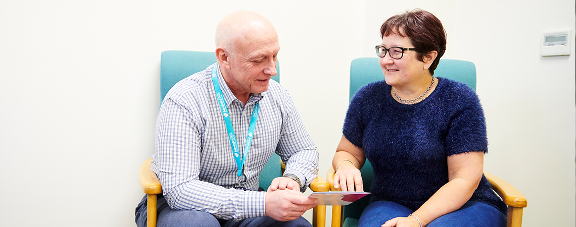 AN Admiral NUrse sitting with a woman sharing a dementia information leaflet