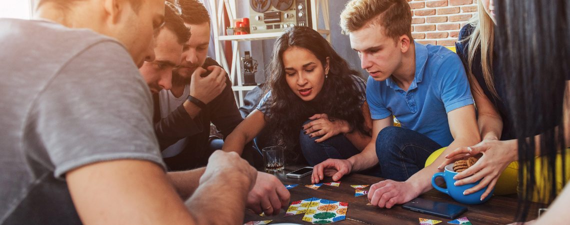 A group of friends play a board game together hunched around a table