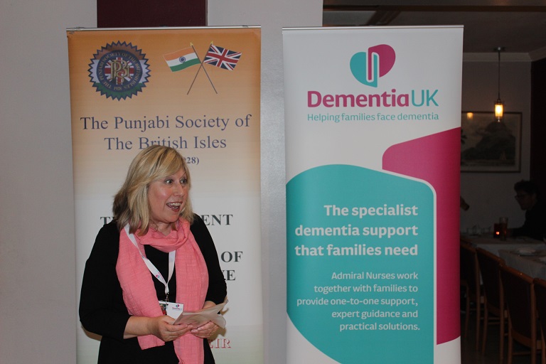 Brenda Foulds speaking at a presentation in front of a Dementia UK banner