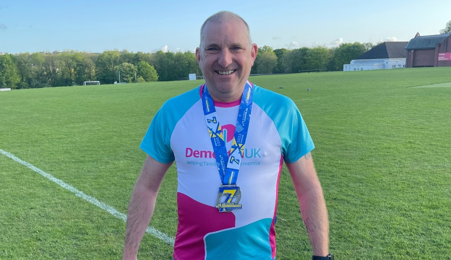 Man standing in a field wearing a Dementia UK T-shirt and a medal