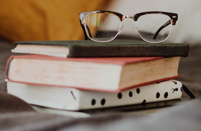 A pair of glasses sits atop a pile of books