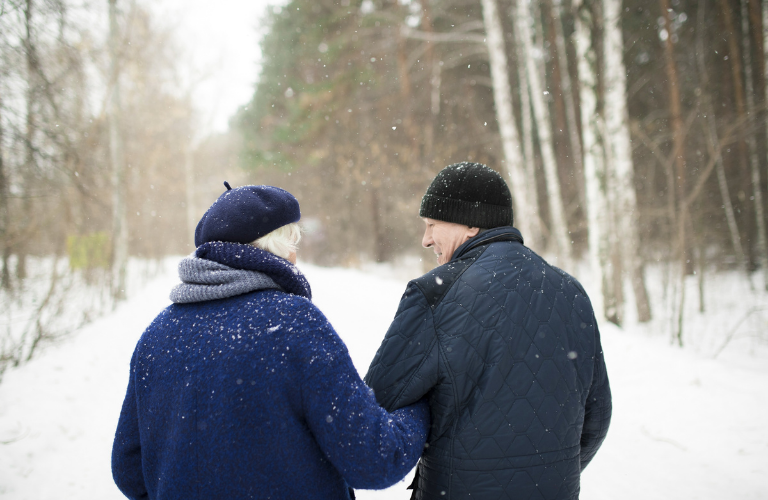 A man and a woman walking through a snowy tree-lined path
