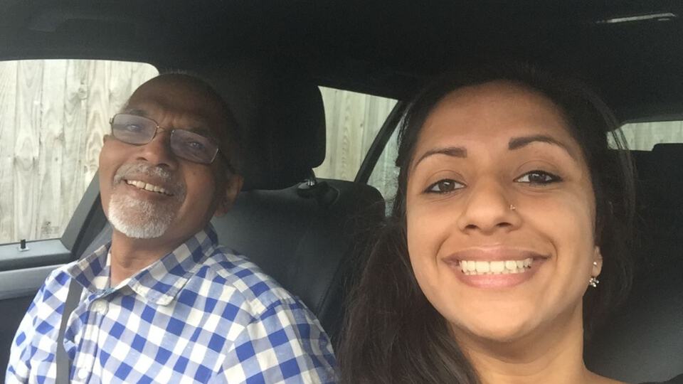 Lady sitting in the car with her Dad. Both smile at the camera