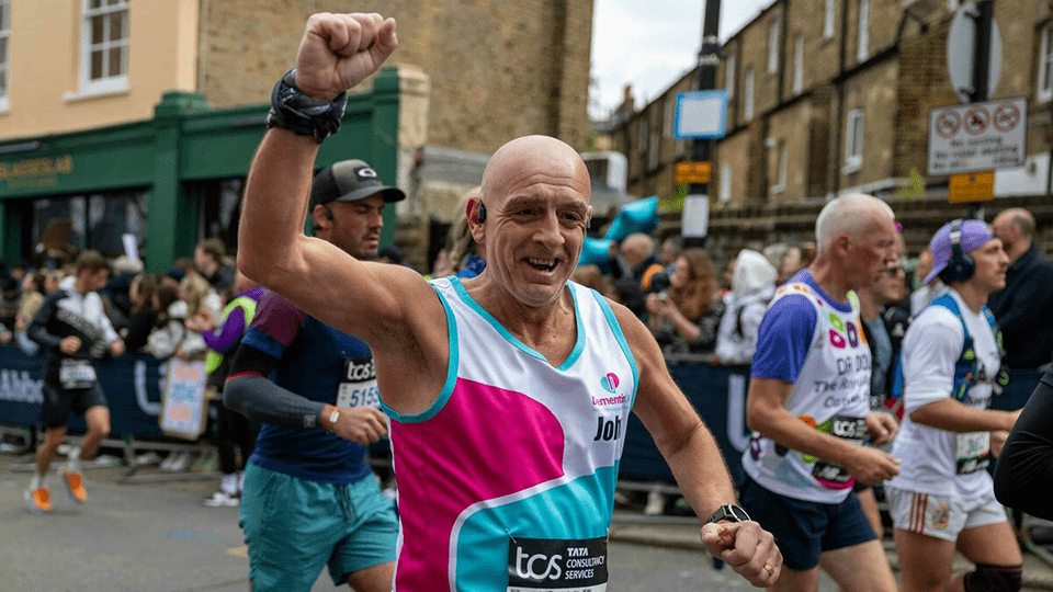 A man smiles to the camera while running a marathon for Dementia UK
