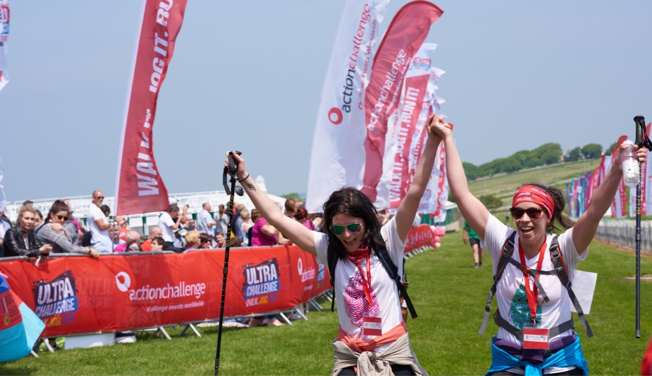 Two women walking using hiking sticks as they near the finish line