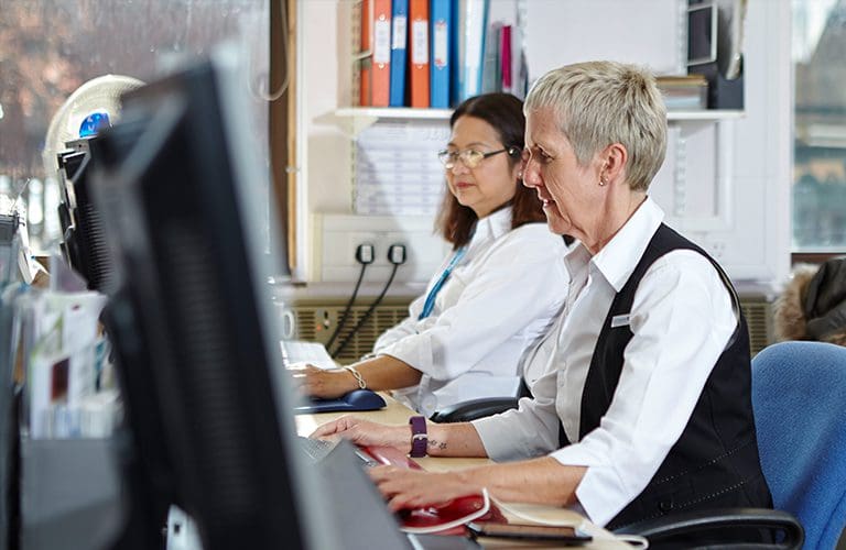 Two Admiral Nurses sitting next to each other at a long desk using computers