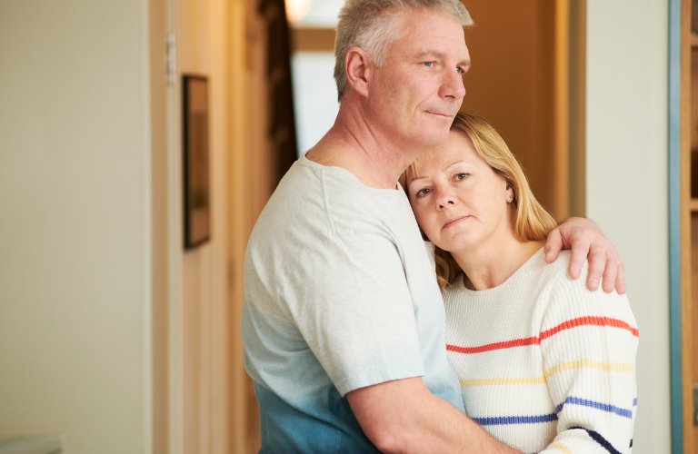 middle-aged couple with forlorn expressions embrace