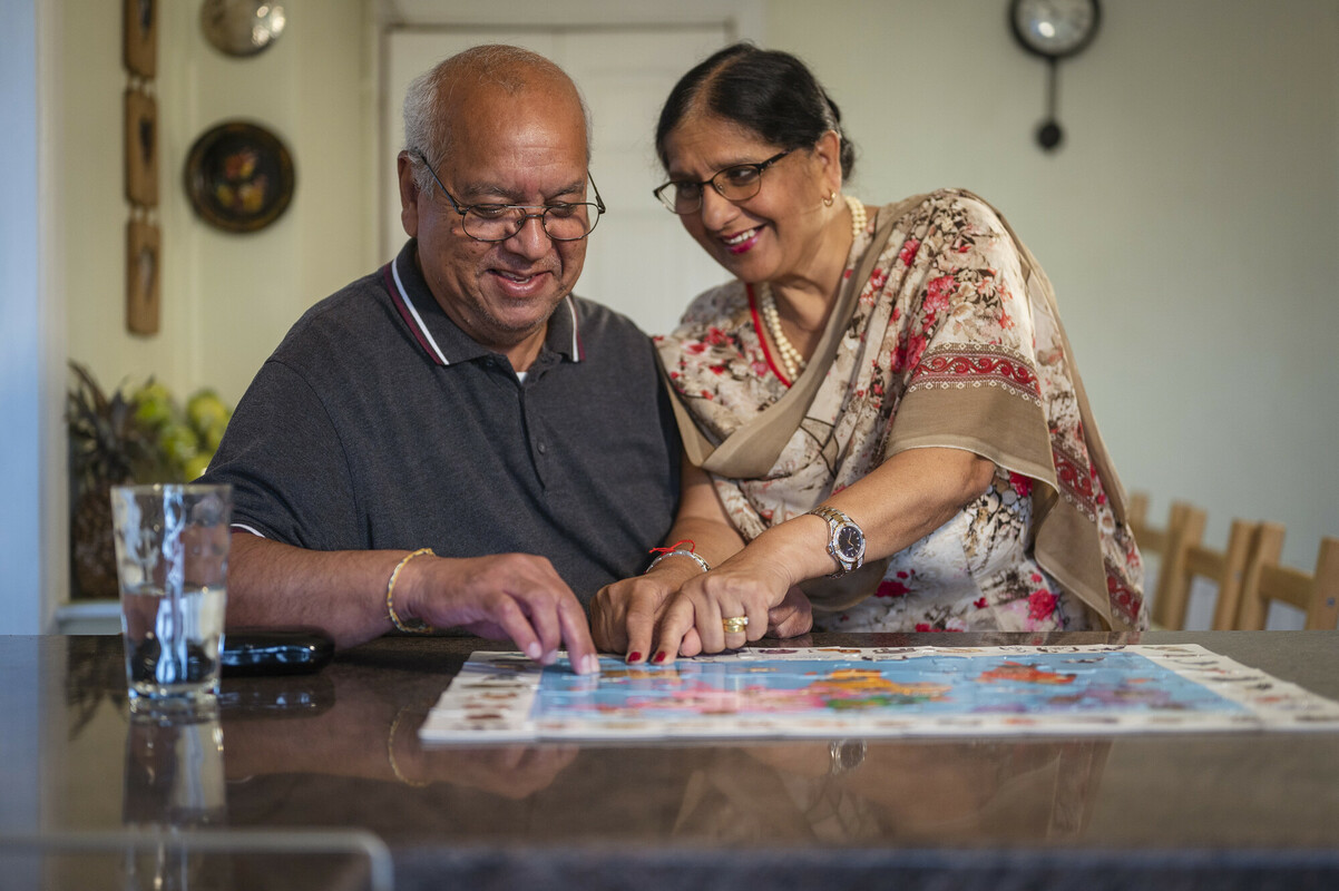 An older man and his wife do a puzzle together indoors.