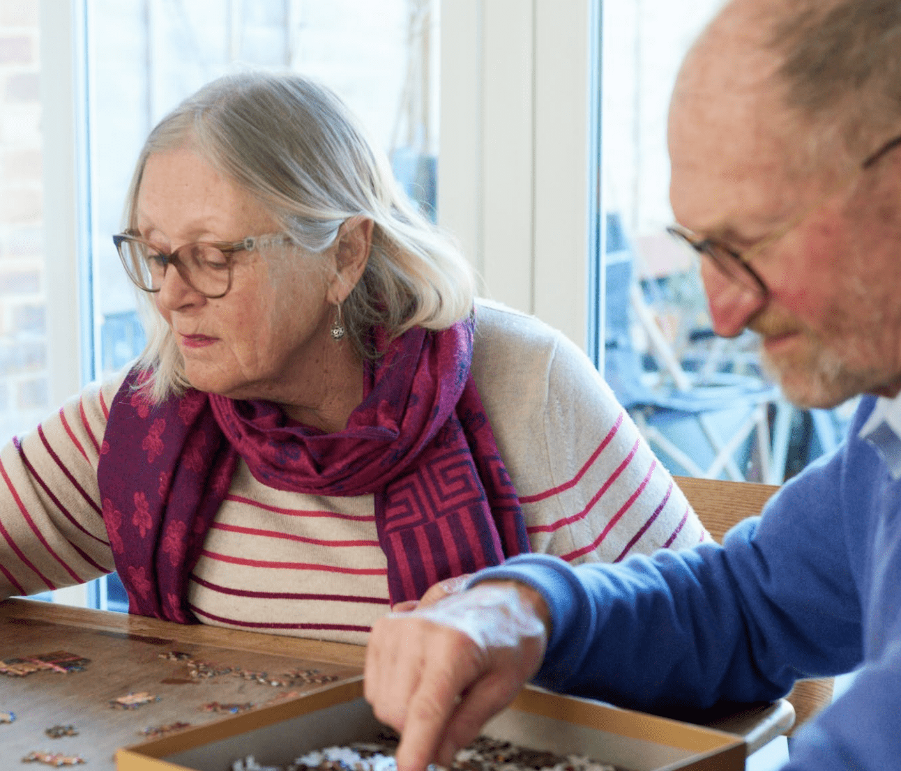 An older couple - a man and woman - do a jigsaw puzzle together at a table