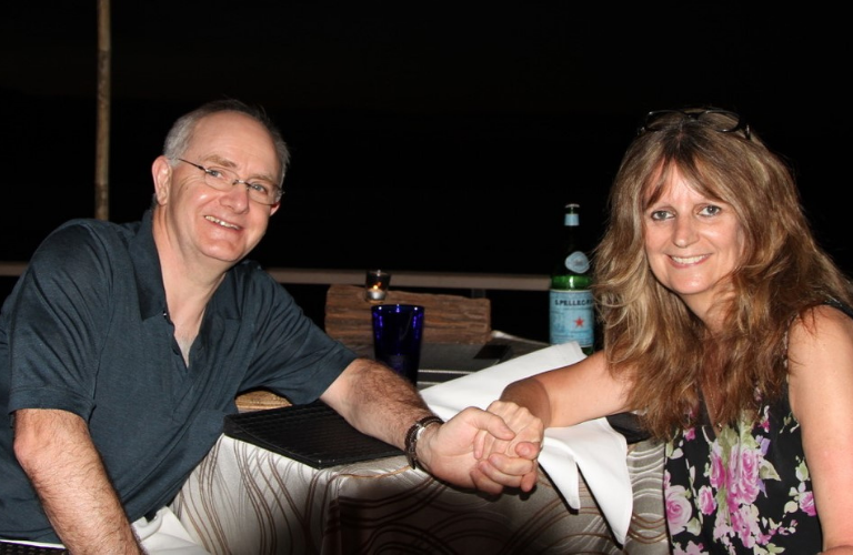 Steve and Julie enjoying evening refreshments by the beach on holiday in 2015