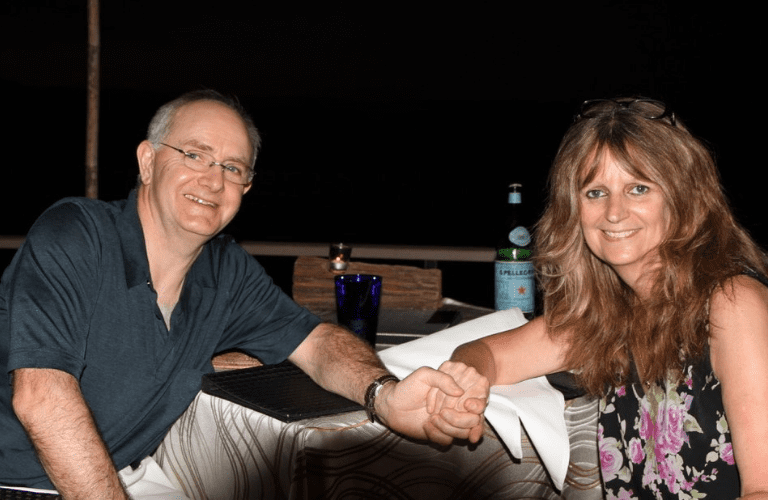 Steve and Julie enjoying evening refreshments by the beach on holiday in 2015