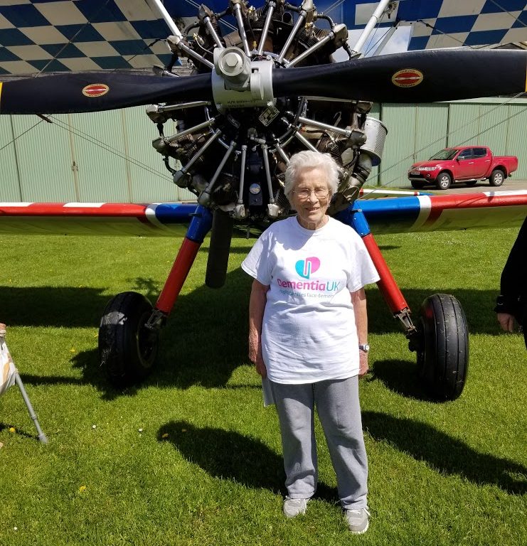 Norma, wearing a Dementia UK t-shirt and standing nex to a plane