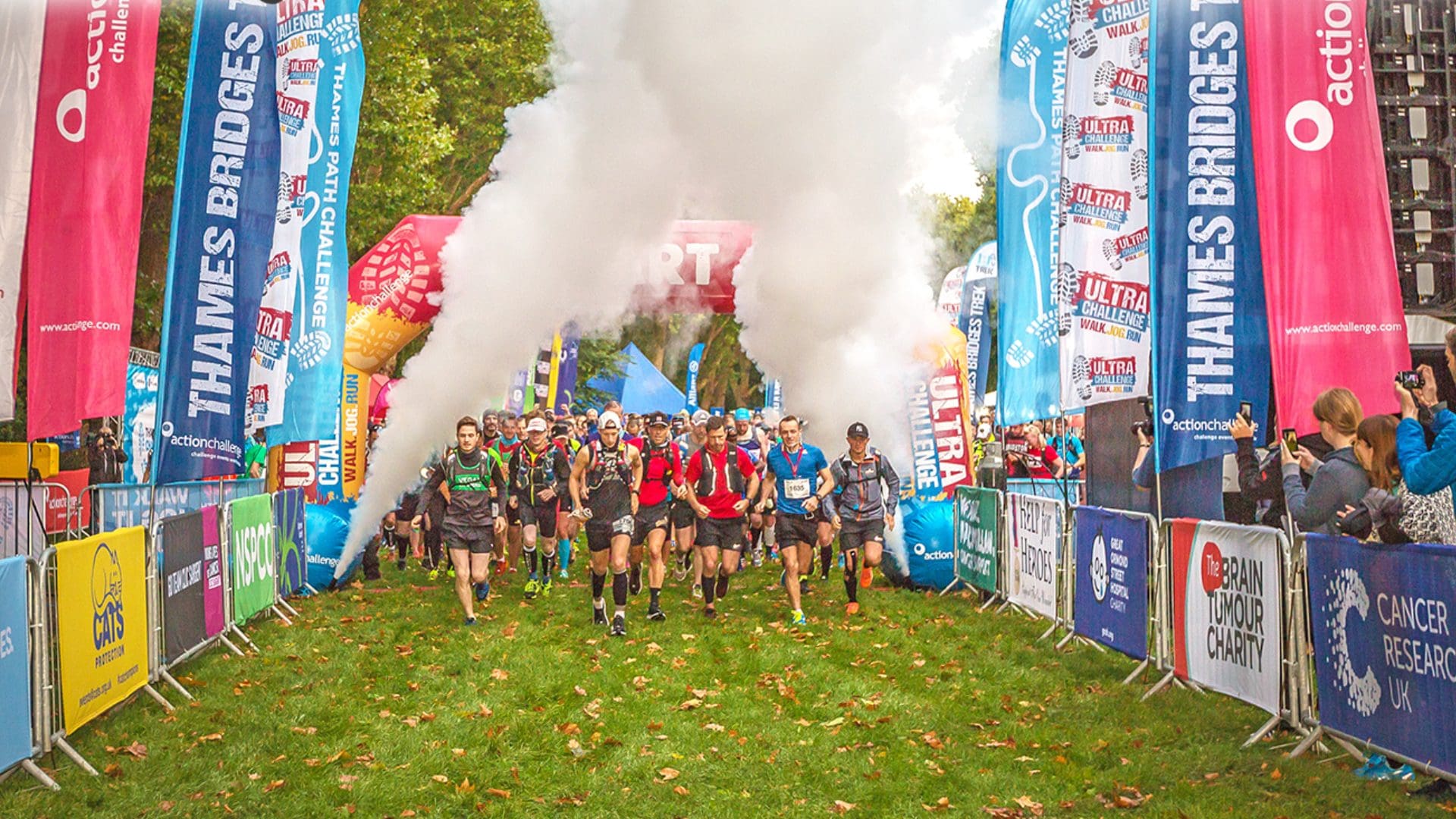 a big group of participants at the start line with flags and smoke behind them