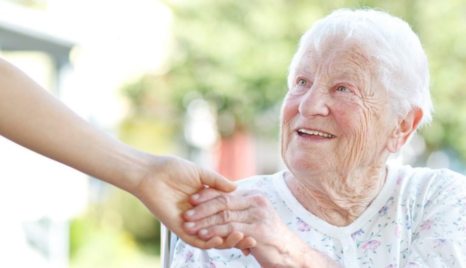 an elderly lady smiling and holding someone's hand