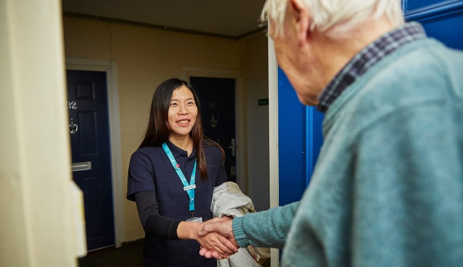 Elderly man opens his front door to welcome a visiting Admiral Nurse. They shake hands