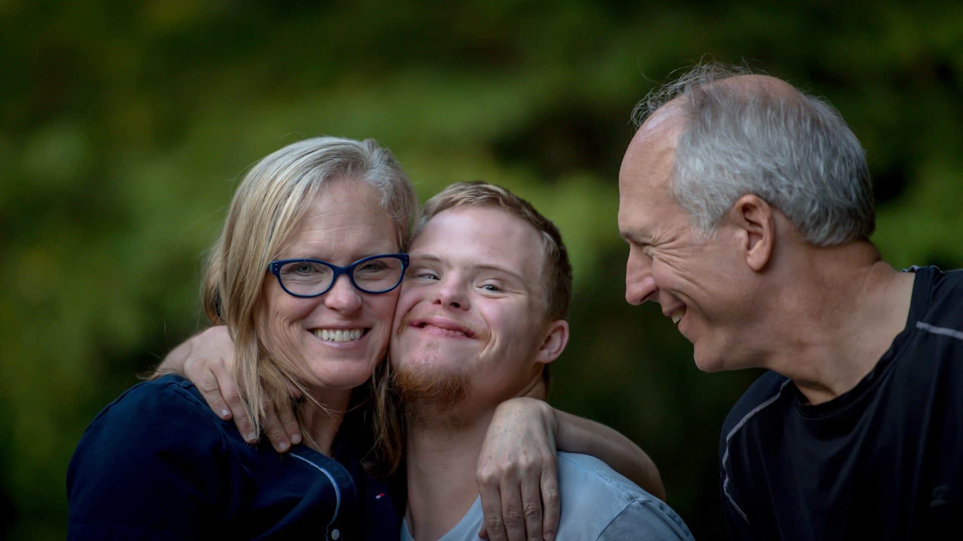 A boy smiles, flanked by two close relatives